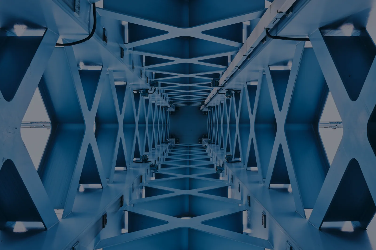 Looking down the inside of a long steel truss bridge, in dark blue and grey.